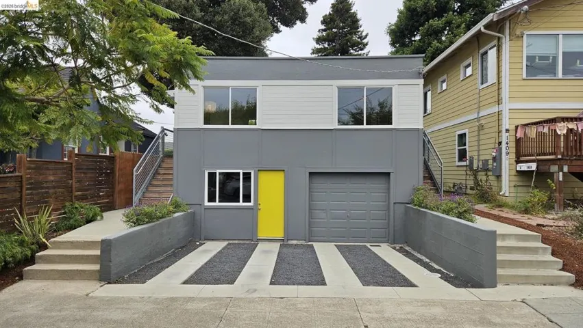 Modern two-story facade featuring a vibrant yellow entry door, an integrated garage, and a concrete driveway with dark aggregate strips