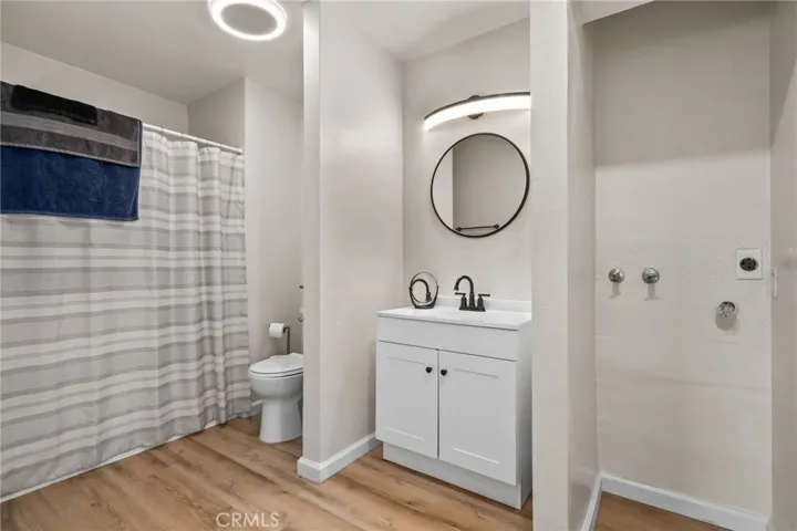 Beautifully updated bathroom with a white shaker vanity, quartz-style counter, matte black fixtures, and a sleek round mirror with modern LED vanity light.