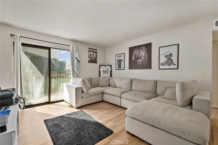 Bright, open-concept living room featuring durable laminate wood flooring, a sliding glass door leading to a private balcony.