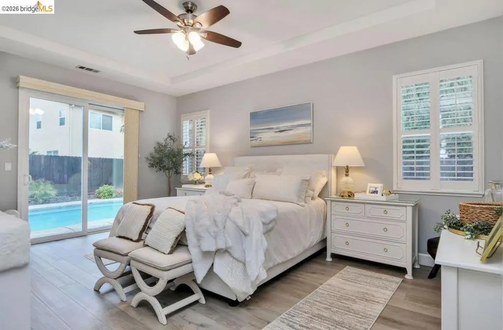 Mater retreat Bedroom featuring light wood-type flooring, a tray ceiling, access to exterior, and a ceiling fan