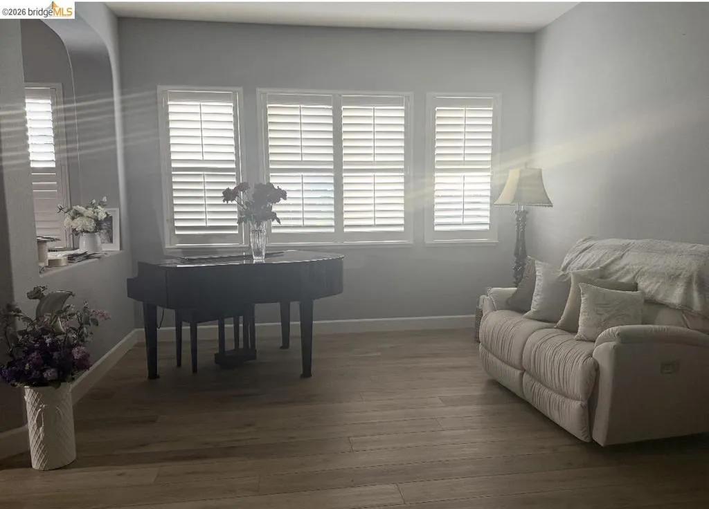 Spacious room featuring wood-finish flooring, three windows with plantation shutters, an arched wall niche, and neutral wall tones
