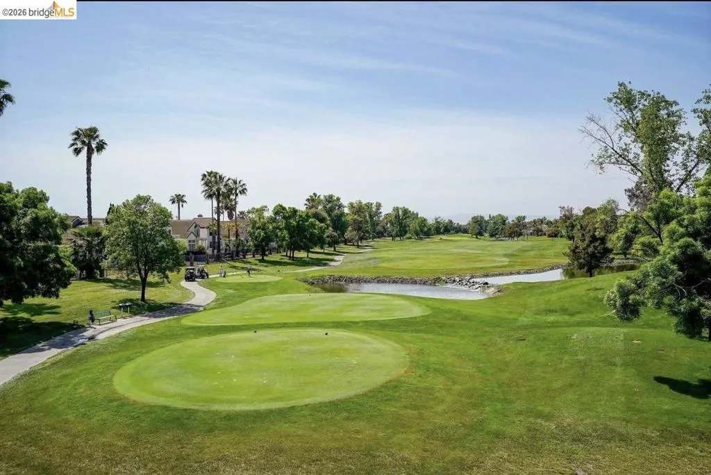 Surrounding community with view of golf course, a water view, view of scattered trees, a lawn, and a putting green