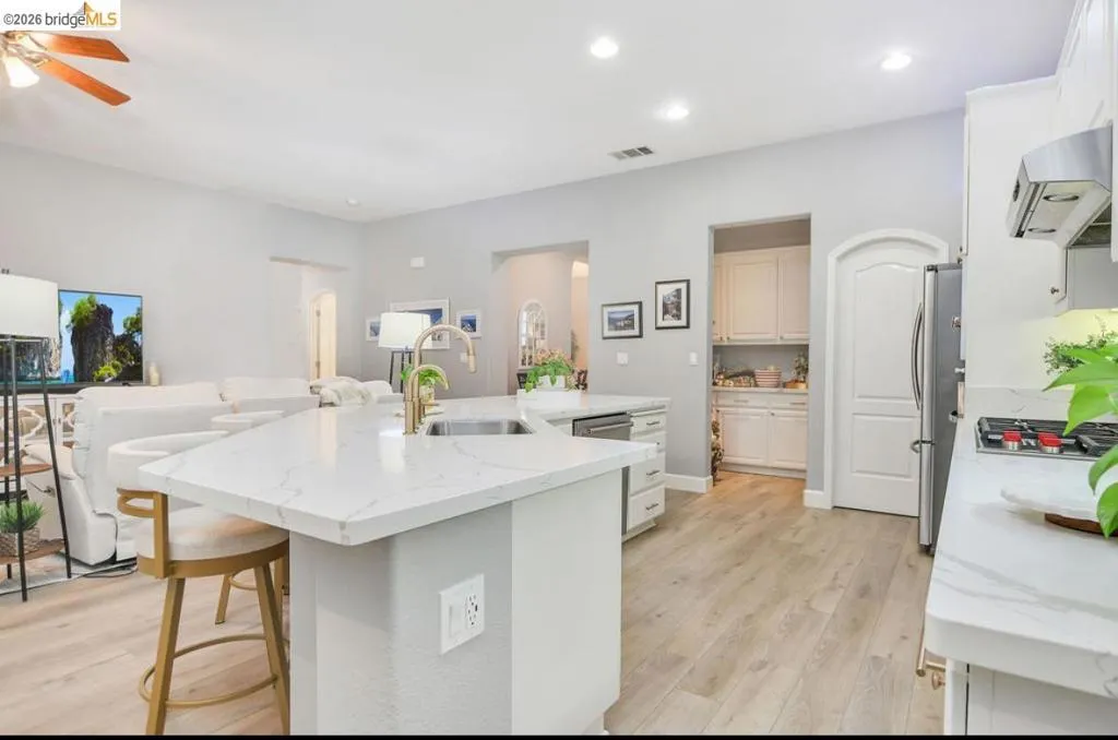 Kitchen with light wood-type flooring, a kitchen breakfast bar, open floor plan, a kitchen island with sink, and light stone counters