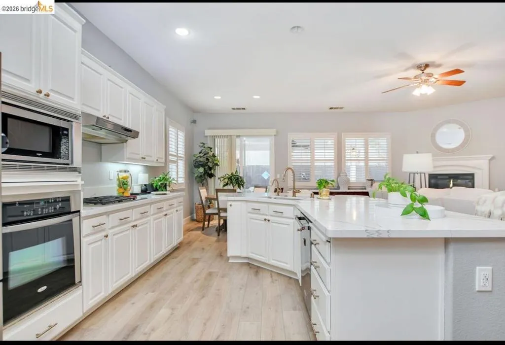 Kitchen featuring appliances with stainless steel finishes, white cabinets, light wood-style flooring, under cabinet range hood, and open floor plan