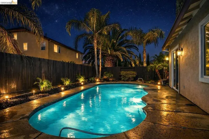 Pool at night featuring a patio and a fenced backyard