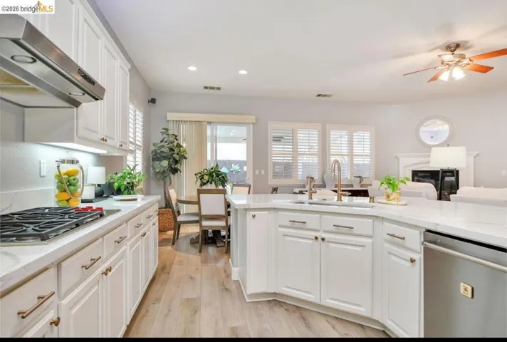 Kitchen with white cabinetry, stainless steel appliances, wall chimney range hood, light stone counters, and recessed lighting