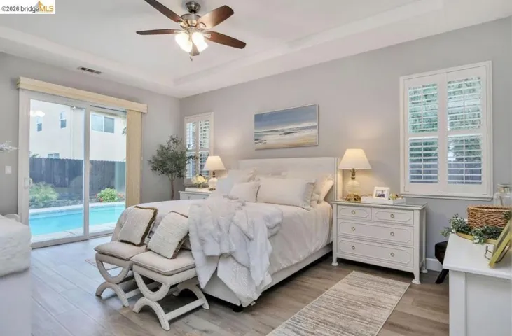 Mater retreat Bedroom featuring light wood-type flooring, a tray ceiling, access to exterior, and a ceiling fan