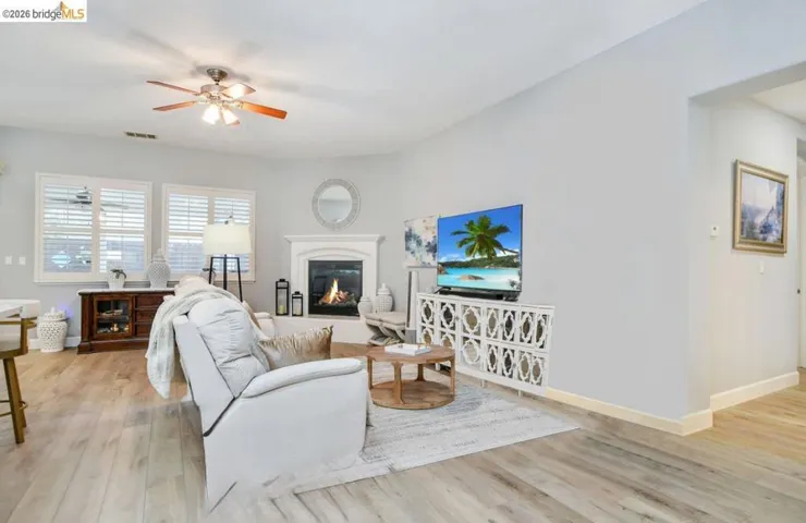 Living room with a glass covered fireplace, ceiling fan, and light wood-style floors