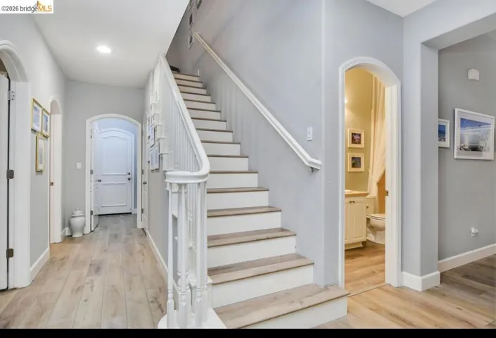 Stairway with arched walkways, wood finished floors, and recessed lighting