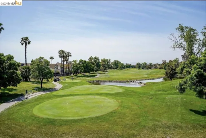 Surrounding community with view of golf course, a water view, view of scattered trees, a lawn, and a putting green