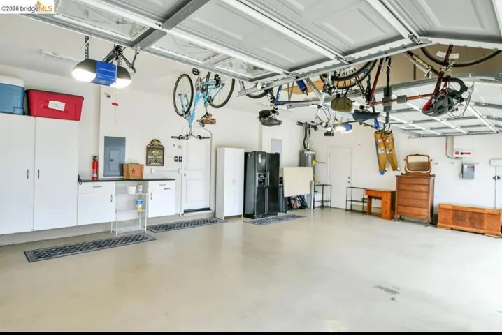 Garage with black refrigerator with ice dispenser, electric panel, and a garage door opener