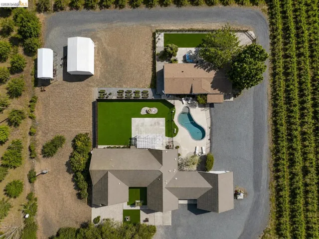 Aerial perspective showcasing a sprawling property featuring a multi-wing residence with a light brown roof, a distinct swimming pool, and extensive paved areas