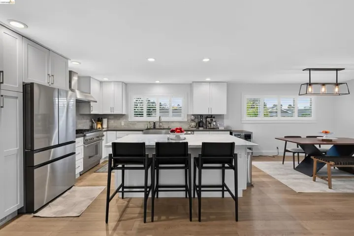 Open-concept kitchen featuring white shaker cabinetry, stainless steel appliances, a center island with seating, and wood-finish flooring