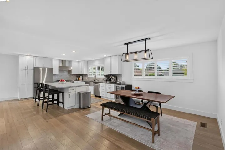 Contemporary kitchen featuring light wood-finish flooring, white cabinetry, a center island with countertop seating, stainless steel appliances, and a tile backsplash