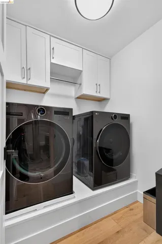 Laundry area featuring light wood-finish flooring, white cabinetry, and a chrome hanging rod