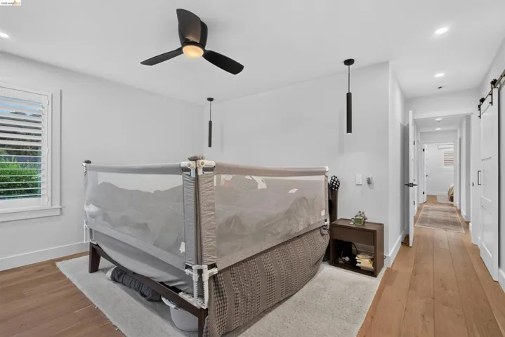 Hardwood-style flooring extends through a bright room with a ceiling fan and recessed lighting