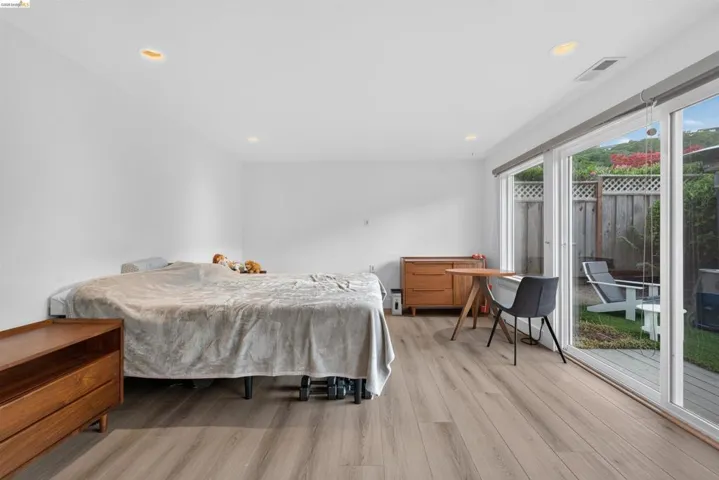 Spacious room featuring wood-finish flooring, recessed ceiling lighting, and expansive sliding glass doors opening to a private outdoor area