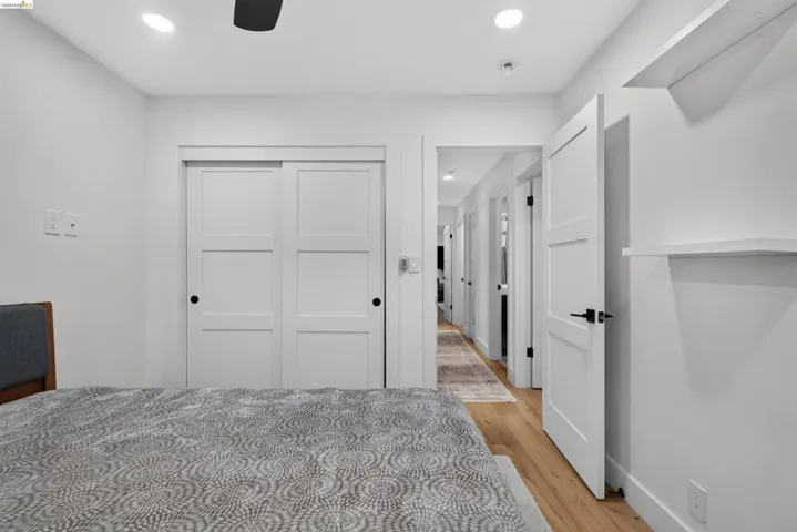 Interior room featuring light wood-finish flooring, white walls, recessed lighting, and a dark ceiling fan