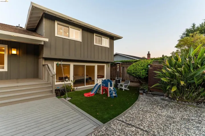 Rear exterior featuring a spacious composite deck, manicured artificial turf, and a pebble-stone pathway