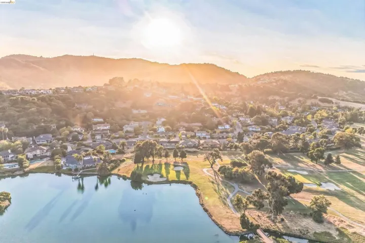 Aerial perspective showcasing a residential community situated alongside a body of water, featuring a golf course and distant hills