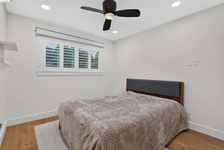 Room featuring wood-finish flooring, recessed lighting, a ceiling fan, white baseboards, and a window with plantation shutters
