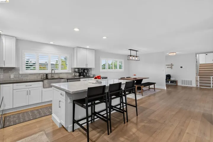 Bright kitchen featuring white shaker cabinetry, an undermount farmhouse sink, and a stone-finish island with seating