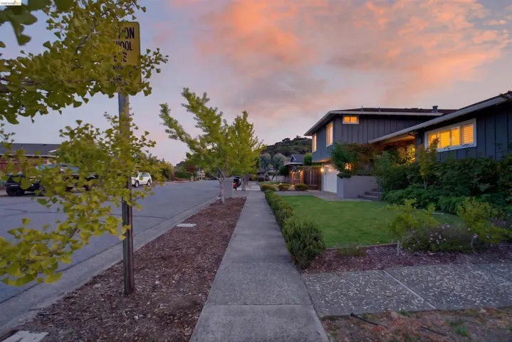 Exterior featuring dark siding, multiple windows, an attached garage, a manicured lawn, and established landscaping