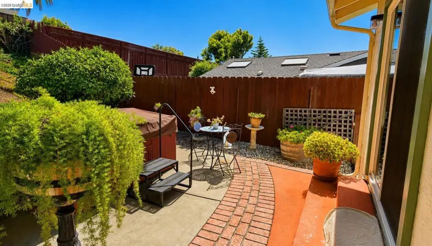Private outdoor patio featuring a hot tub, brick pathway, and mature landscaping