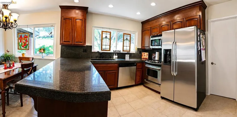 Kitchen featuring a curved peninsula with a dark countertop, recessed lighting, wood cabinetry, stainless steel appliances, and tile flooring