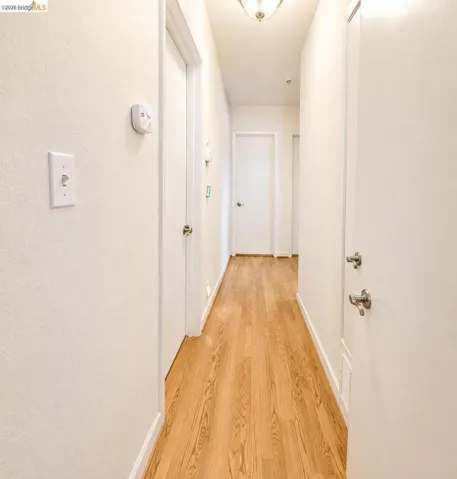 Hardwood-finish flooring in a bright hallway, featuring white walls, white baseboards, and multiple interior doors with brushed nickel hardware
