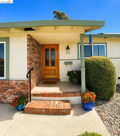Entryway featuring a wood-panel door with decorative glass inserts, brick-accented facade, concrete porch, and brick steps with a black metal handrail