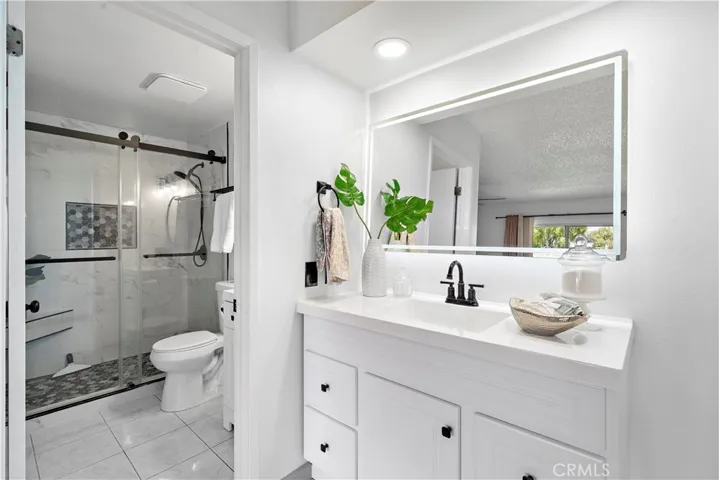 Primary Ensuite Bathroom is beautiful remodeled ensuite bathroom with two quartz vanities with newer light fixtures, and a walk-in shower with sitting bench, shampoo niche, designer tile surround and barndoor style clear glass enclosure