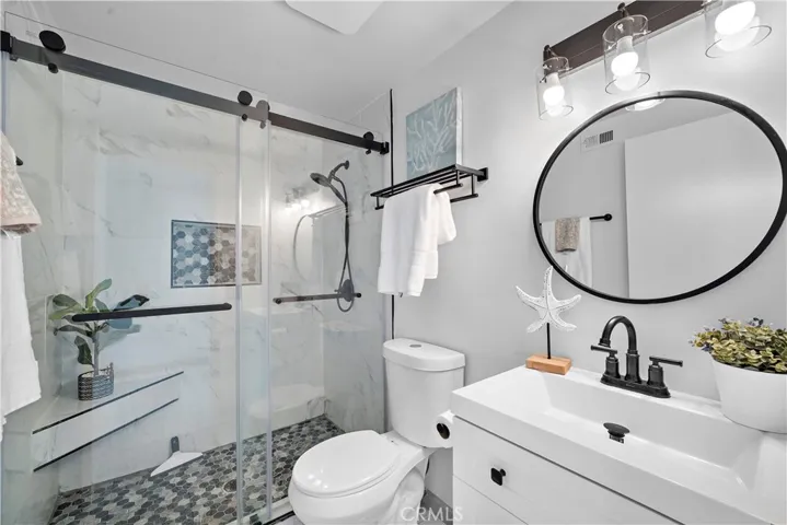 Remodeled ensuite bathroom with two quartz vanities with newer light fixtures, and a walk-in shower with sitting bench, shampoo niche, designer tile surround and barndoor style clear glass enclosure