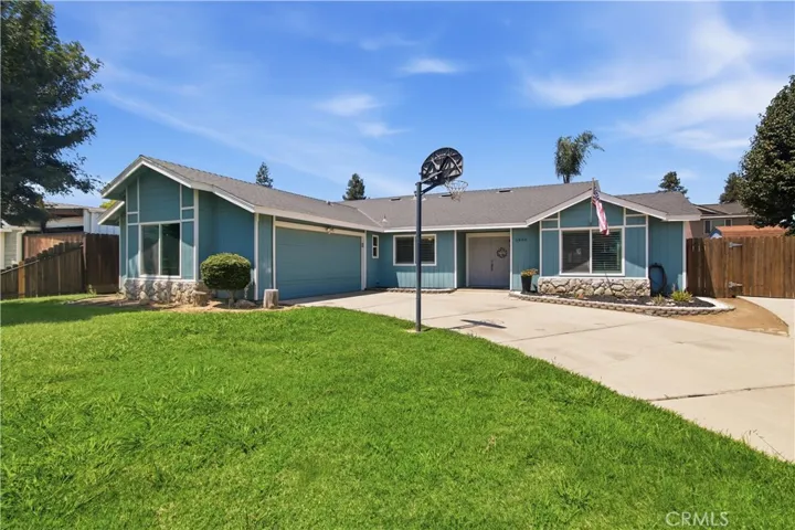 Blue ranch style home with large driveway and basketball hoop