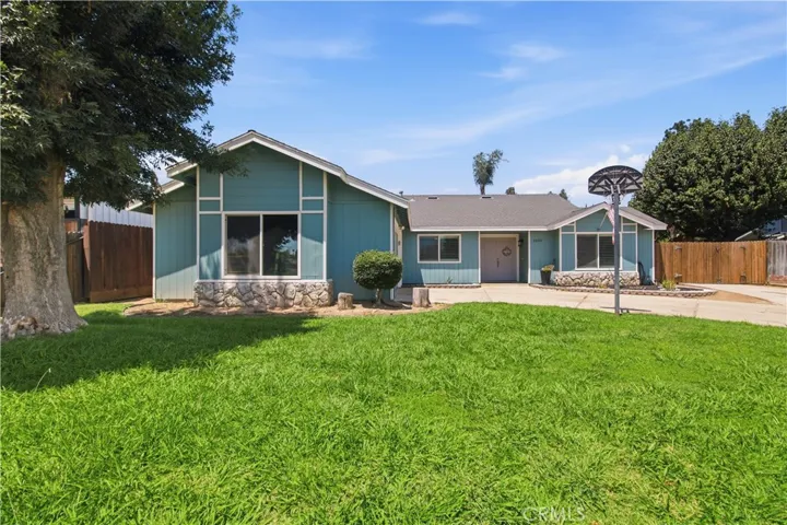 Blue ranch style home with large driveway and basketball hoop