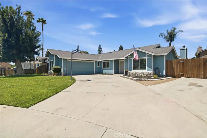 Blue ranch style home with large driveway and basketball hoop