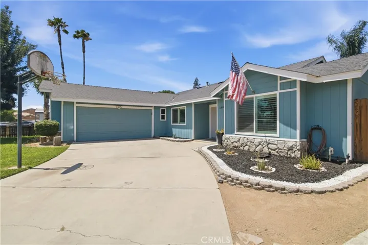 Blue ranch style home with large driveway and basketball hoop