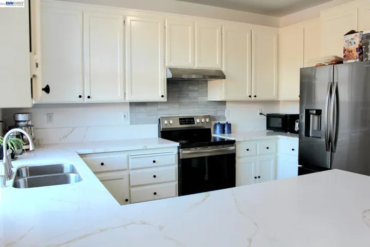 Thoughtfully updated kitchen with expansive quartz counters, white shaker-style cabinetry, stainless steel appliances, and generous workspace. Clean finishes and abundant storage create a timeless, inviting space.