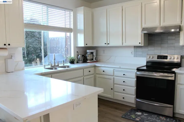 Modern kitchen with sleek quartz countertops, white cabinetry, stainless steel appliances, and a spacious layout. Large window over the sink fills the space with natural light and enhances the bright, airy feel.