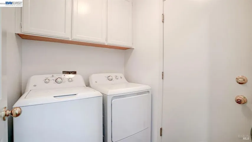 Dedicated indoor laundry room featuring side-by-side washer and dryer hookups, overhead storage cabinets, and convenient access, making everyday household tasks simple and organized.