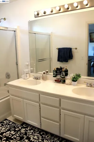 Primary bathroom features a dual-sink vanity, expansive mirror, generous cabinet storage, and a glass-enclosed shower, offering a bright and functional space for everyday use.