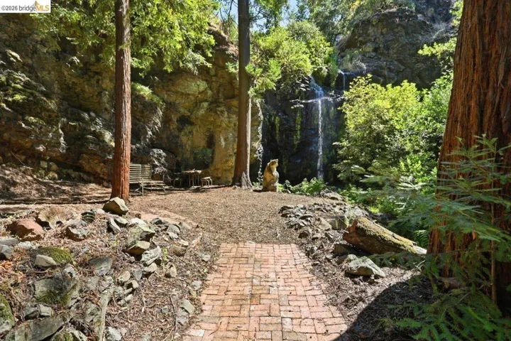 Natural rock formations frame a private outdoor space featuring a brick pathway, mature redwood trees, and a waterfall