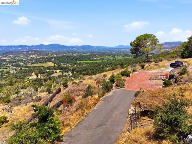 Expansive mountain and valley scenery featuring an asphalt drive, level paved area, and a mature tree