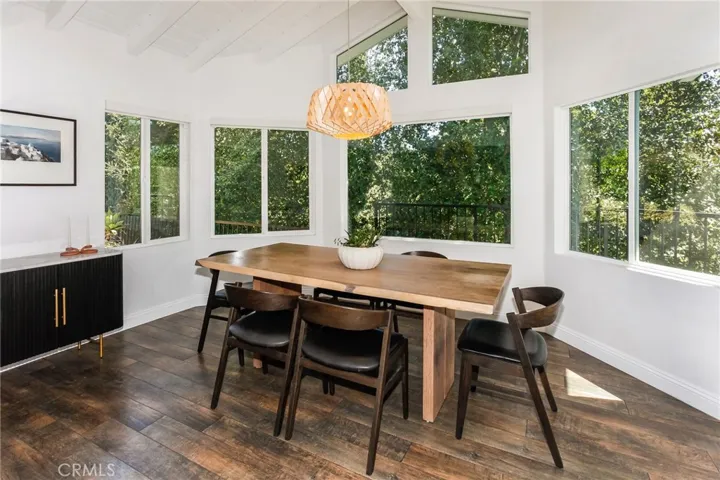 The kitchen flows effortlessly into both the dining room and family room, creating a welcoming space for everyday living and entertaining. The adjacent dining room features a pitched beamed ceiling, designer lighting, expansive picture windows, motorized solar blinds, and direct access to the deck and garden.