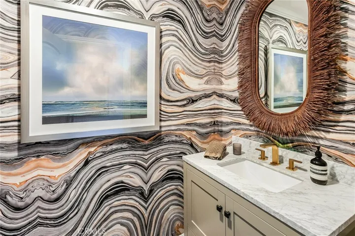 A stylish powder room featuring designer wallpaper, marble topped vanity, and an Anteriors mirror adds a distinctive touch for guests.