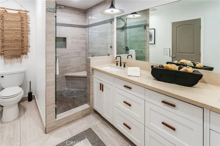 The en suite bath features dual sinks, a quartz topped vanity, designer lighting, tiled flooring, and a glass-enclosed custom walk-in shower.