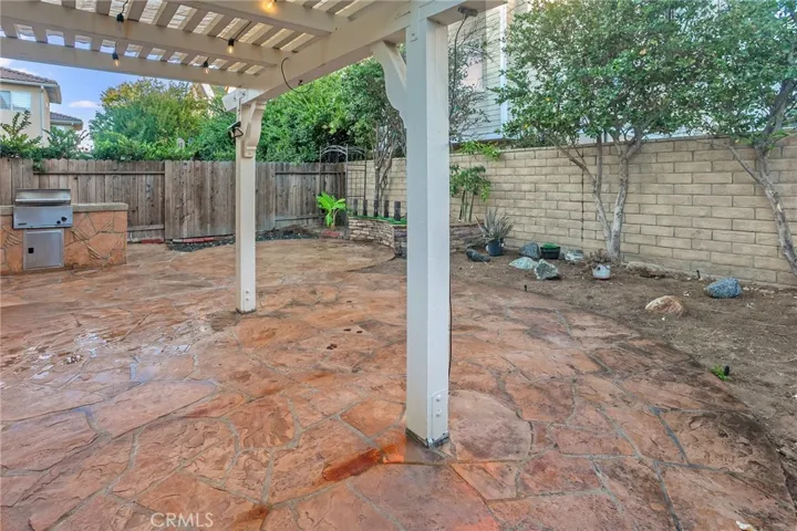 The backyard is designed for easy enjoyment with a pergola-covered stone patio, built-in barbecue, open patio, raised planters, and orange, papaya, and banana trees.