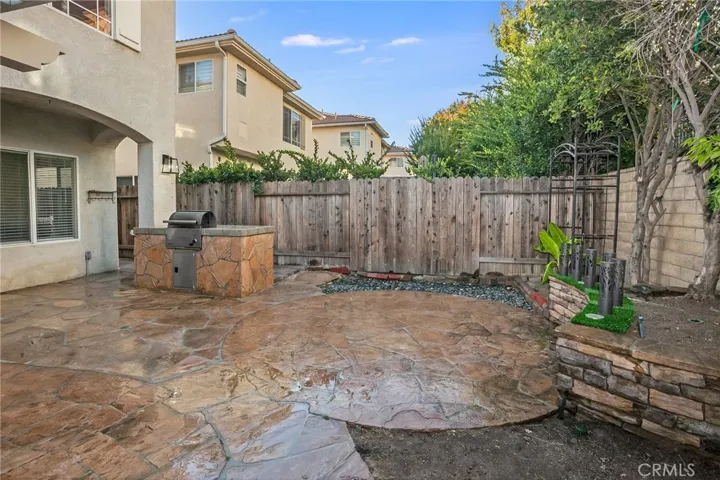 The backyard is designed for easy enjoyment with a pergola-covered stone patio, built-in barbecue, open patio, raised planters, and orange, papaya, and banana trees.