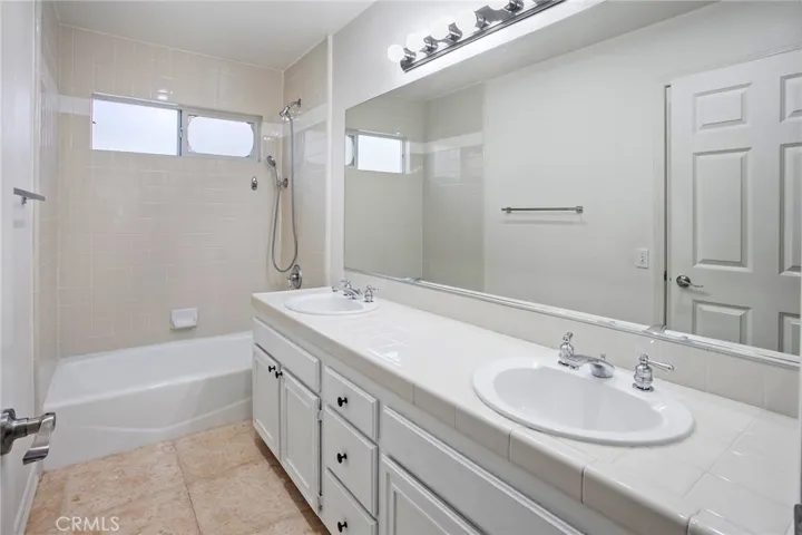 Full guest bathroom with glass enclosed tub/shower and dual basins.
