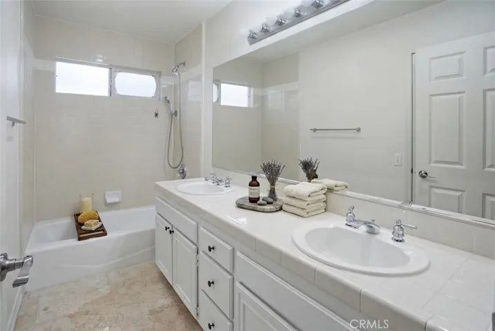 Photo is virtually staged.  Previous photo is how property currently shows. Full guest bathroom with glass enclosed tub/shower and dual basins.
